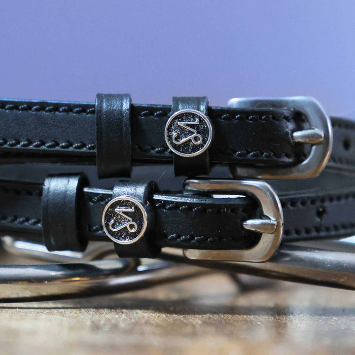 Close-up of round Capricorn zodiac medallion charms on black leather spur straps