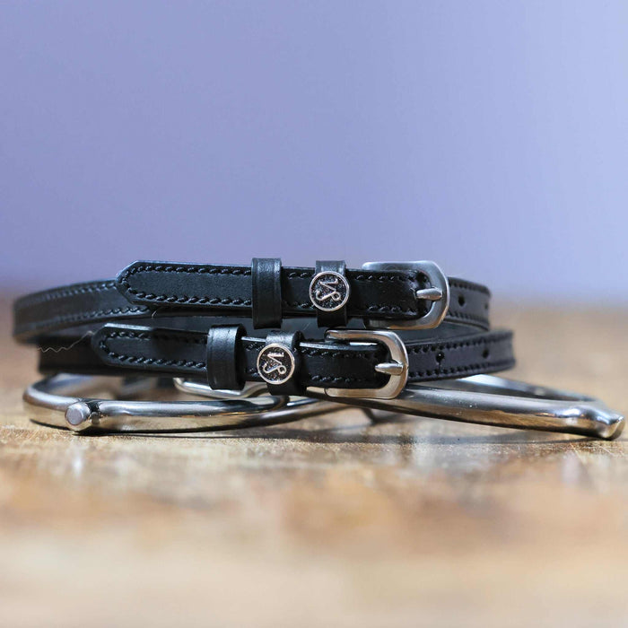Black Capricorn zodiac spur straps coiled beside a silver spur, purple backdrop