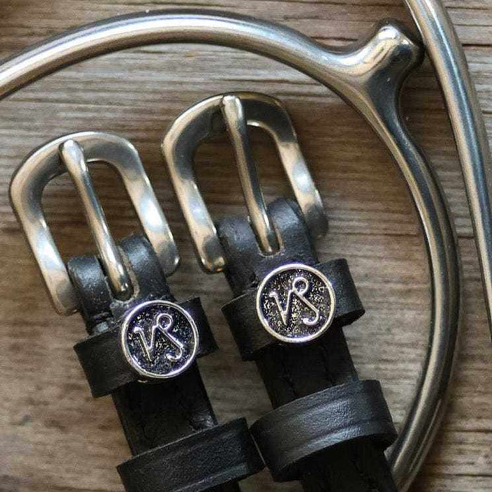 Close-up of Capricorn zodiac charm spur straps on weathered wood beside a spur