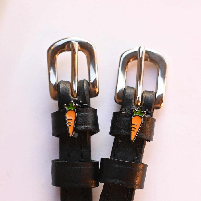 Silver buckles and carrot charms on black leather spur straps, close-up on a pink background