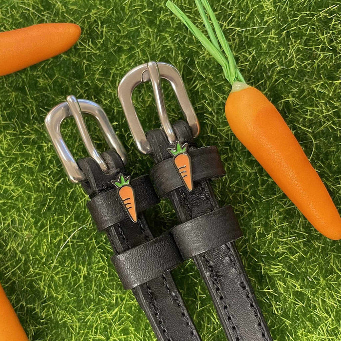 Black leather carrot spur straps styled on grass beside real and toy carrots by ManeJane