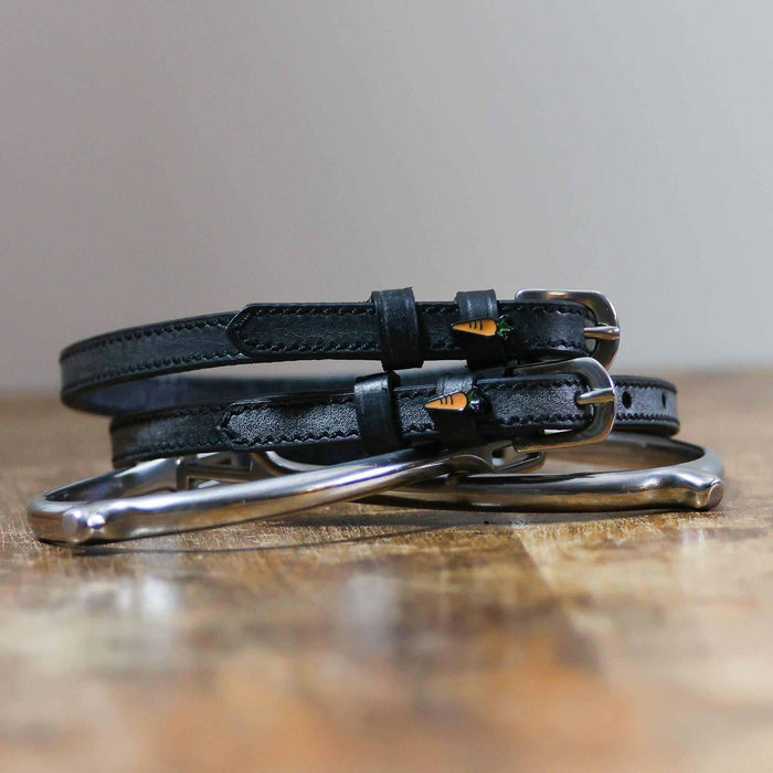 Coiled black leather ManeJane carrot spur straps stacked on a spur on a wooden table