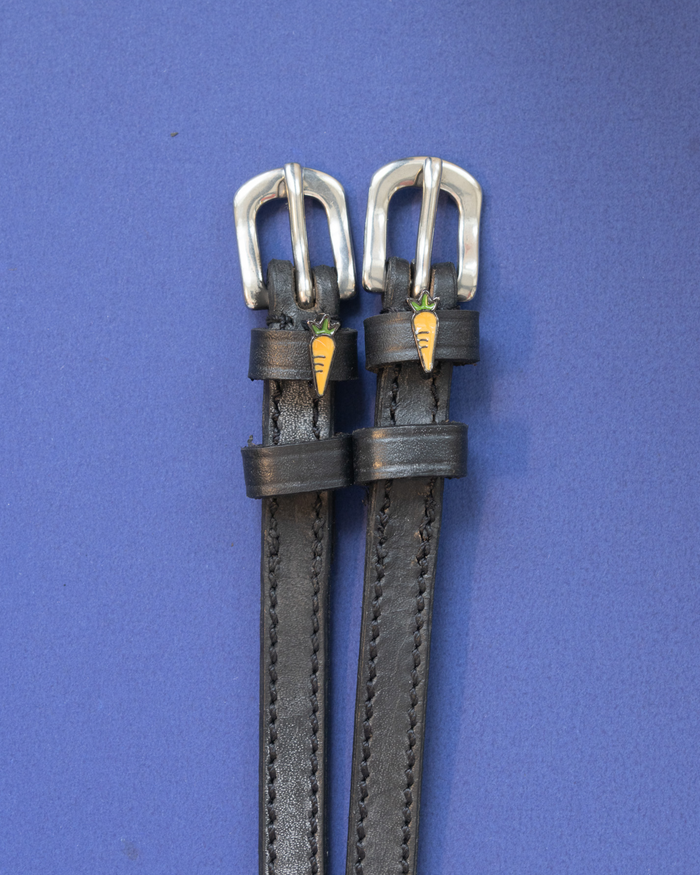 Pair of black leather spur straps with silver buckles and carrot charms on a blue background