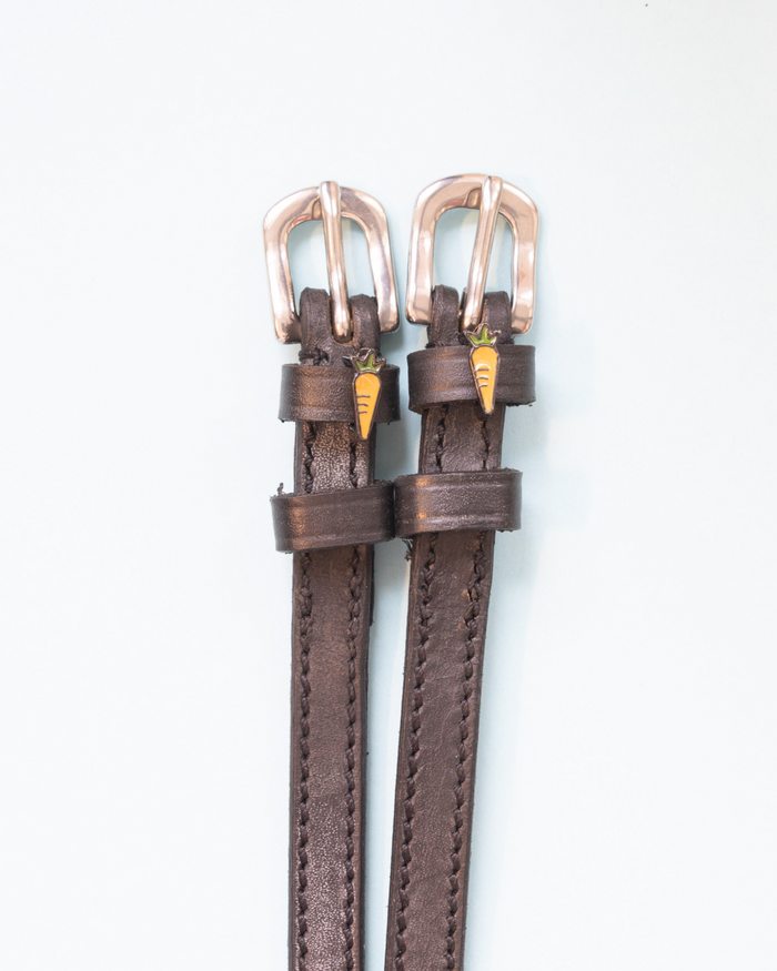 Brown leather spur straps with rose gold buckles and carrot charms on white by ManeJane