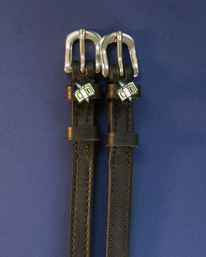 Black leather cash money spur straps flat-laid on a navy background
