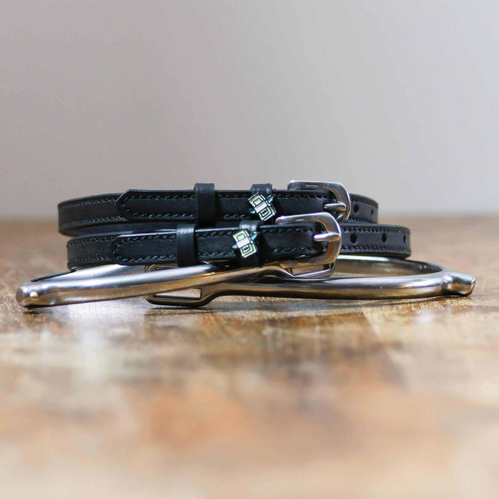 Black leather cash money spur straps coiled beside a spur on wood