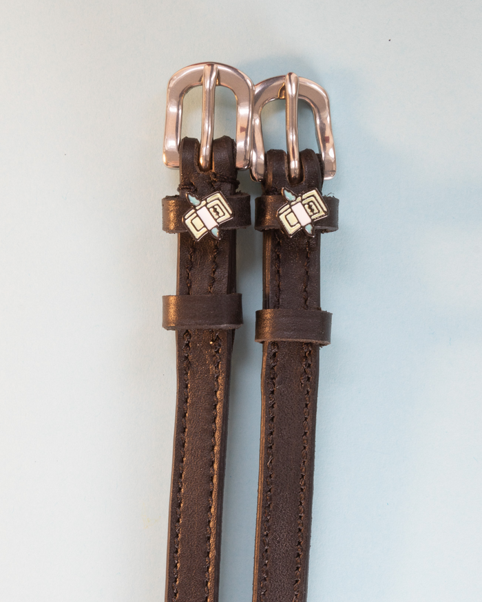 Dark brown leather cash money spur straps with rose-gold buckles on grey