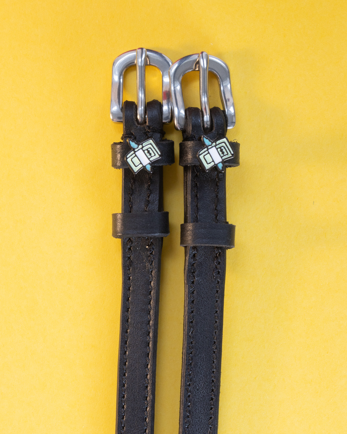 Black leather cash money spur straps flat-laid on a yellow background