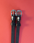 Black leather ManeJane spur straps with champagne-glass charms on a coral background