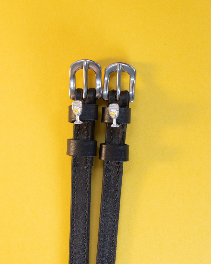Pair of champagne-glass spur straps laid flat on a yellow background