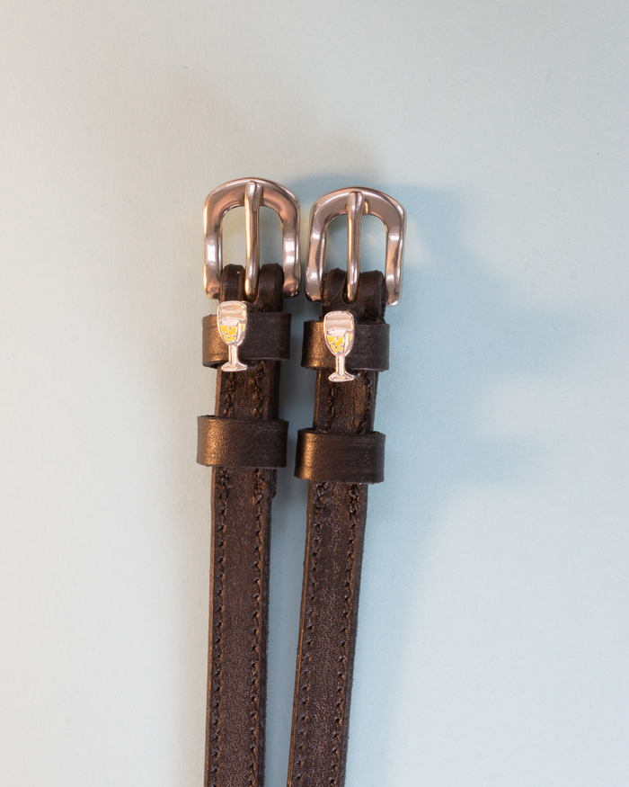 Brown leather spur straps with champagne-glass charms and brass buckles