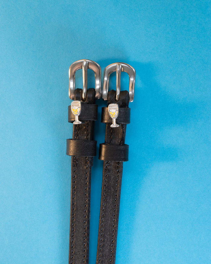 Black leather champagne spur straps laid flat on a bright blue background