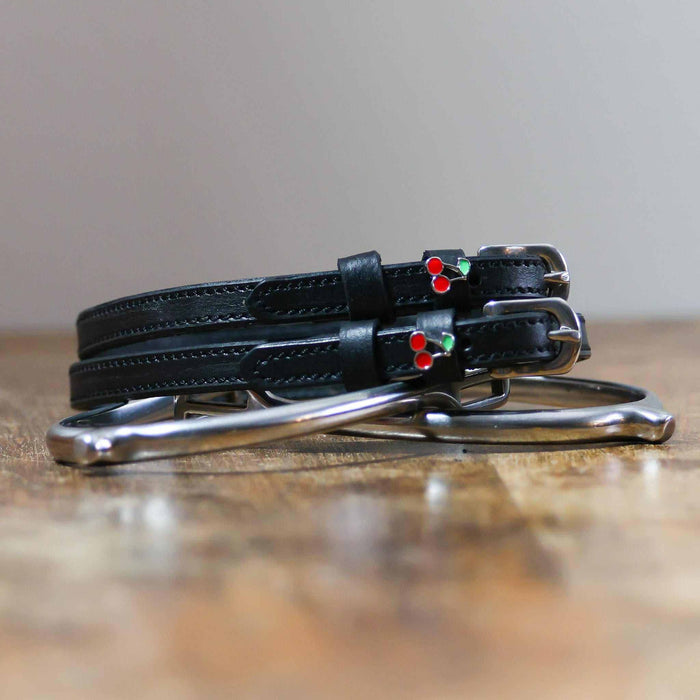 Black leather cherry spur straps coiled beside a metal spur on a wooden surface