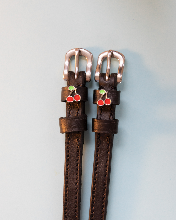 Dark brown leather ManeJane cherry spur straps with rose-gold buckles on pale blue
