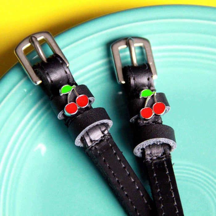Black leather cherry charm spur straps resting on a teal and yellow dish