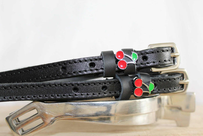 Black leather cherry spur straps laid over a silver spur on a white surface