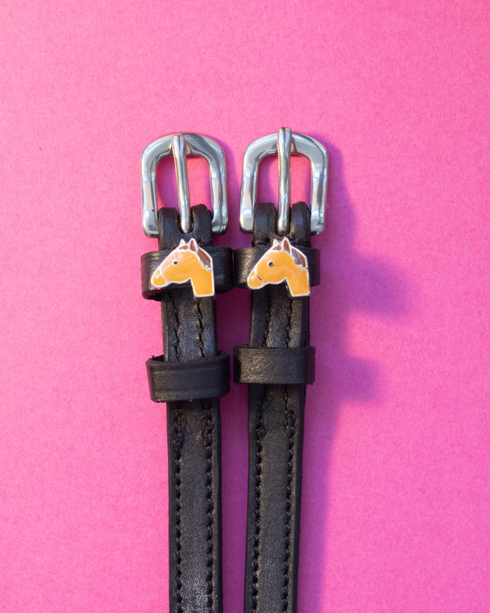 Black leather ManeJane spur straps with chestnut horse-head charms on hot pink