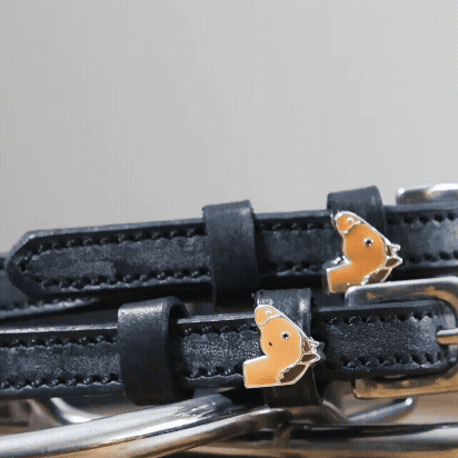 Close-up of chestnut horse-head charms on black leather spur strap keepers
