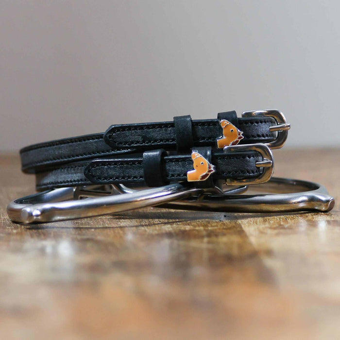 Coiled black leather spur straps and a silver spur on wood with chestnut horse charms
