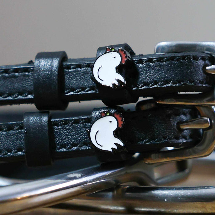 Close-up of white enamel chicken charms on black leather ManeJane spur strap keepers