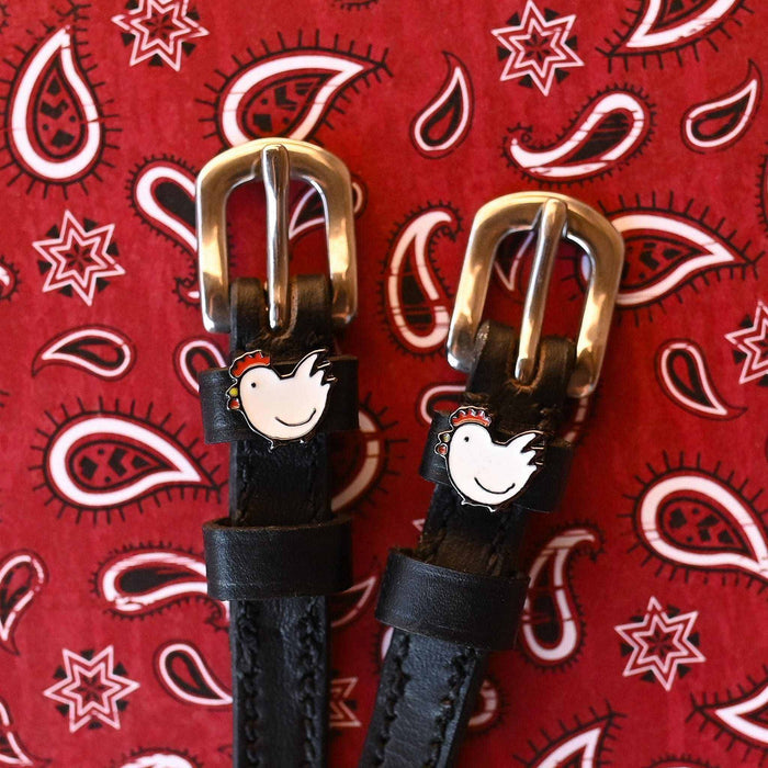 Black leather chicken spur straps with brass buckles on a red paisley bandana background