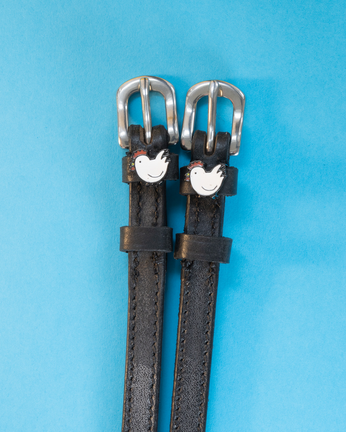 Black leather chicken spur straps with silver buckles on a light blue background