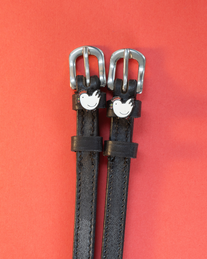 Black leather chicken spur straps with silver buckles on a coral red background