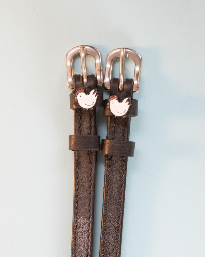 Brown leather ManeJane chicken spur straps with rose-gold buckles on pale blue