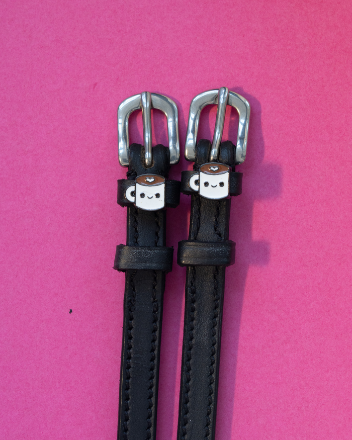 Black leather ManeJane spur straps with smiling coffee-mug charms on pink