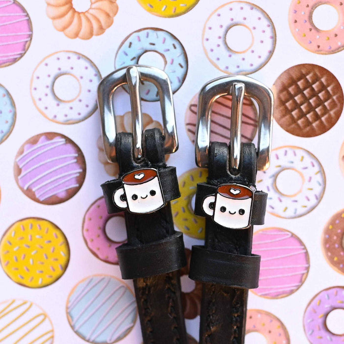 Coffee-mug charm spur straps on a donut-print backdrop, buckle close-up