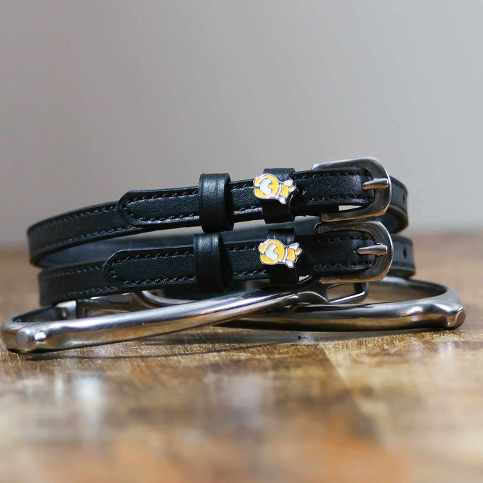 Black leather corgi butt spur straps coiled beside a spur on wood