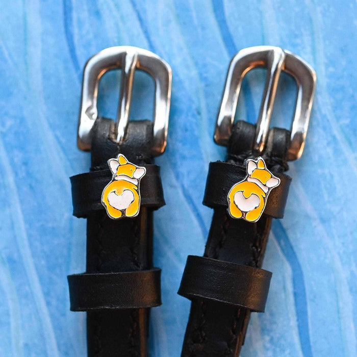 Two corgi butt charms on black leather spur straps over blue texture