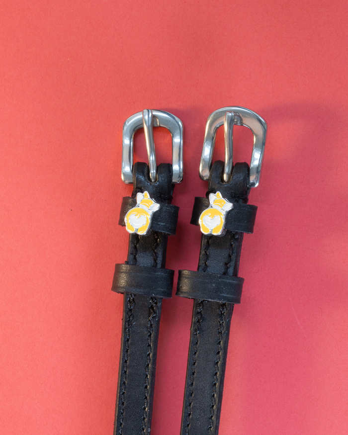 Pair of black leather corgi butt spur straps on a coral background