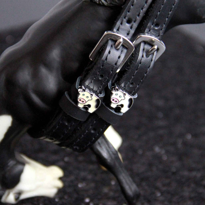 Black leather cow spur straps fastened on a model horse's leg, ManeJane enamel cow charm detail