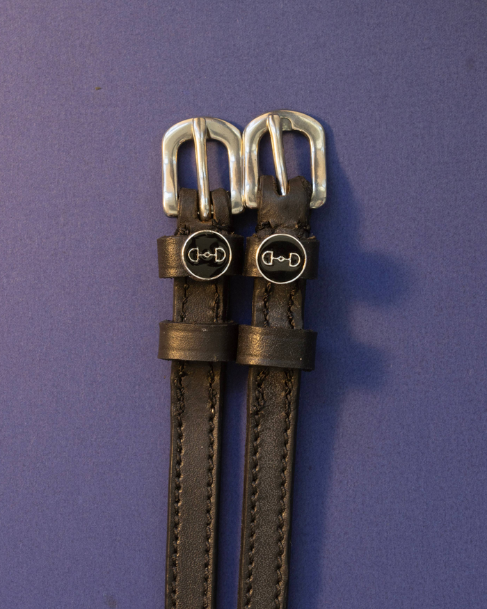 Black leather bit-charm spur straps laid flat on a purple background