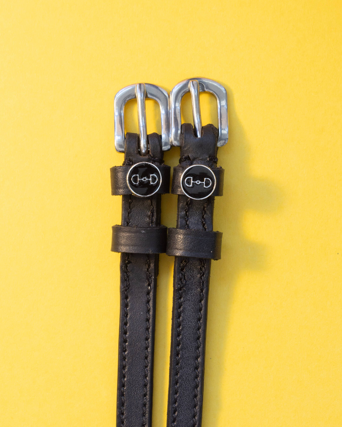 Pair of snaffle-bit charm spur straps laid flat on a yellow background