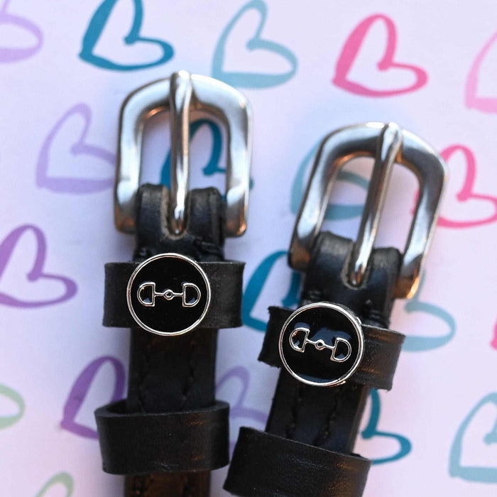 D-ring bit charm spur straps on a pastel heart-doodle backdrop, buckle close-up