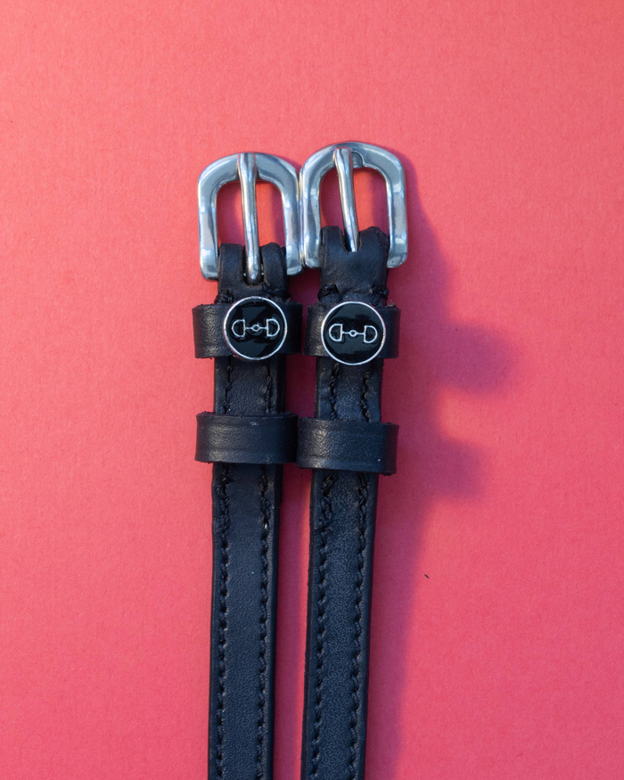 Black leather spur straps with round bit charms flat on a red background