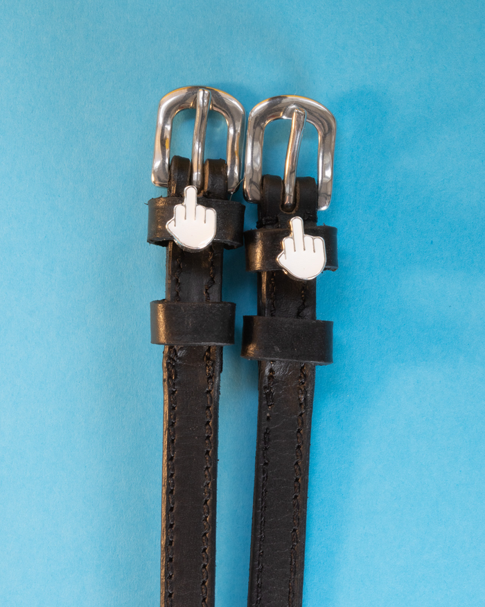 Black leather ManeJane Da Bird spur straps with white middle-finger emoji charms on a blue background