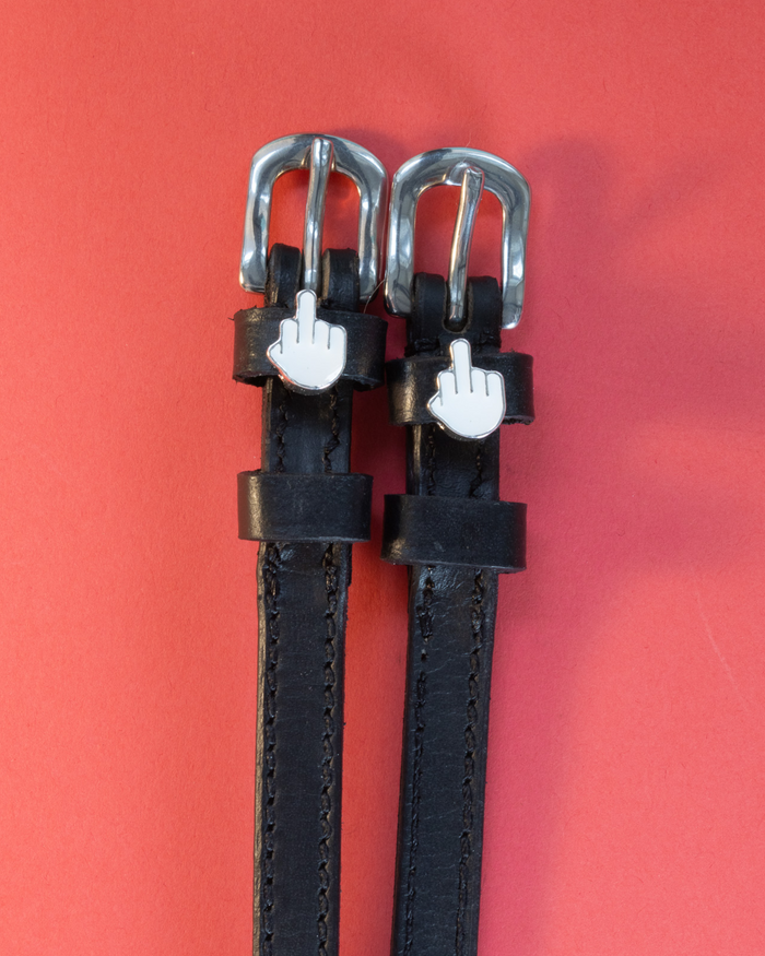 Black leather Da Bird spur straps with white middle-finger emoji charms on a coral background