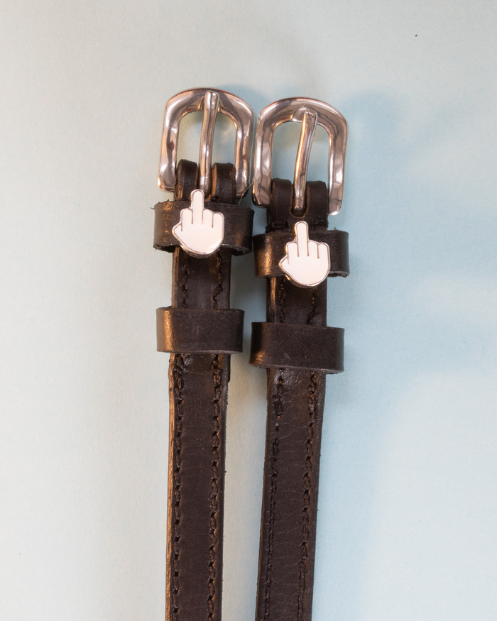 Black leather Da Bird spur straps with white middle-finger charms on a pale blue background