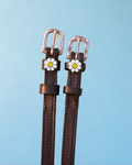 Dark brown leather ManeJane spur straps with silver buckles and white daisy charms on blue