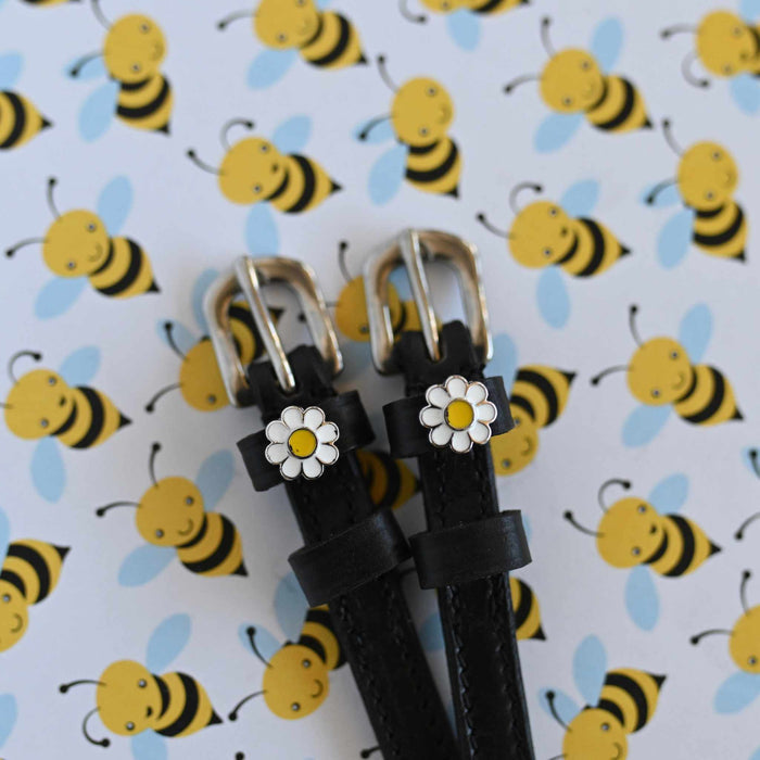 White daisy charm spur straps with silver buckles against a cartoon bee print backdrop