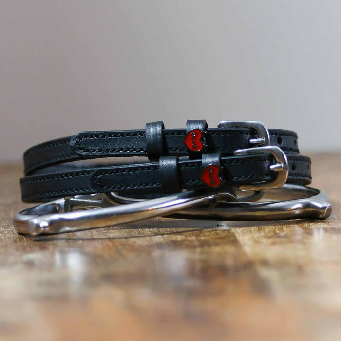 Black Devil heart spur straps coiled around a silver spur on a wooden surface