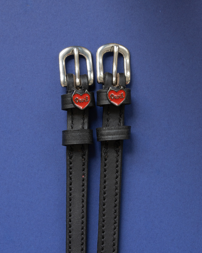 Pair of black leather Devil heart spur straps flat-laid on a royal blue background