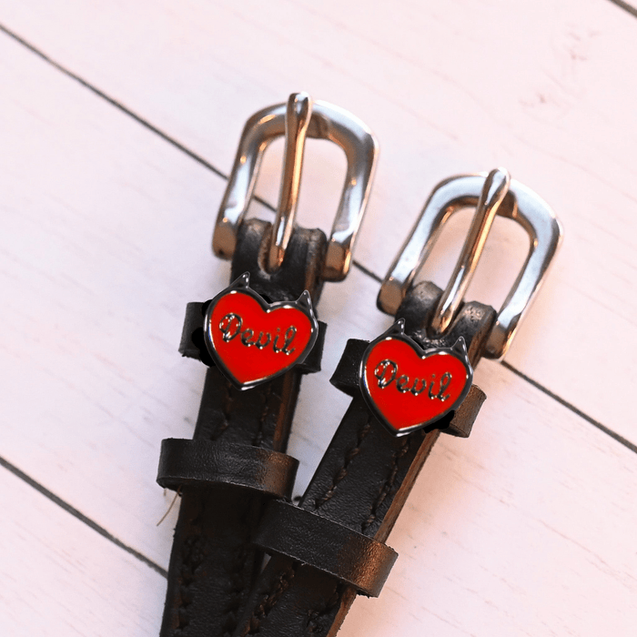 Red Devil heart charms on black spur straps against white-washed wood planks