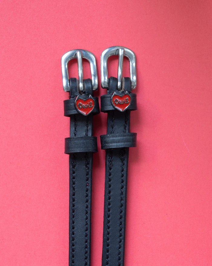 Black leather Devil heart spur straps with silver buckles on a coral background