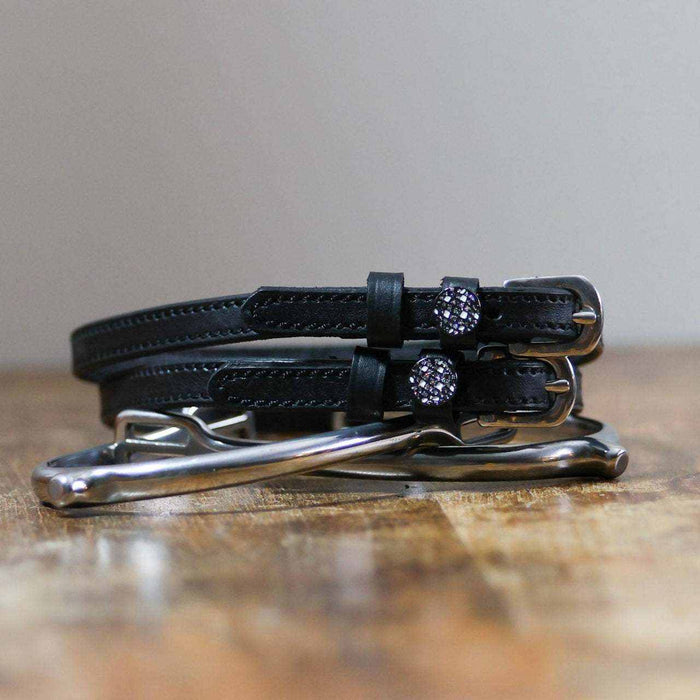 Black leather disco ball spur straps coiled beside a silver spur on a wood surface