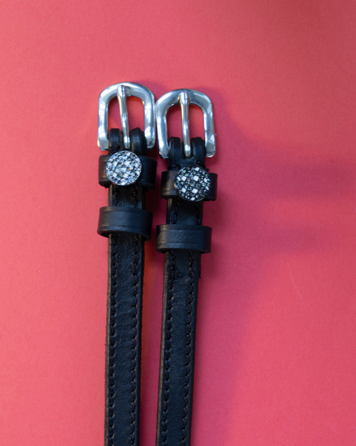 Sparkling disco ball spur straps in black leather with silver buckles on a red background