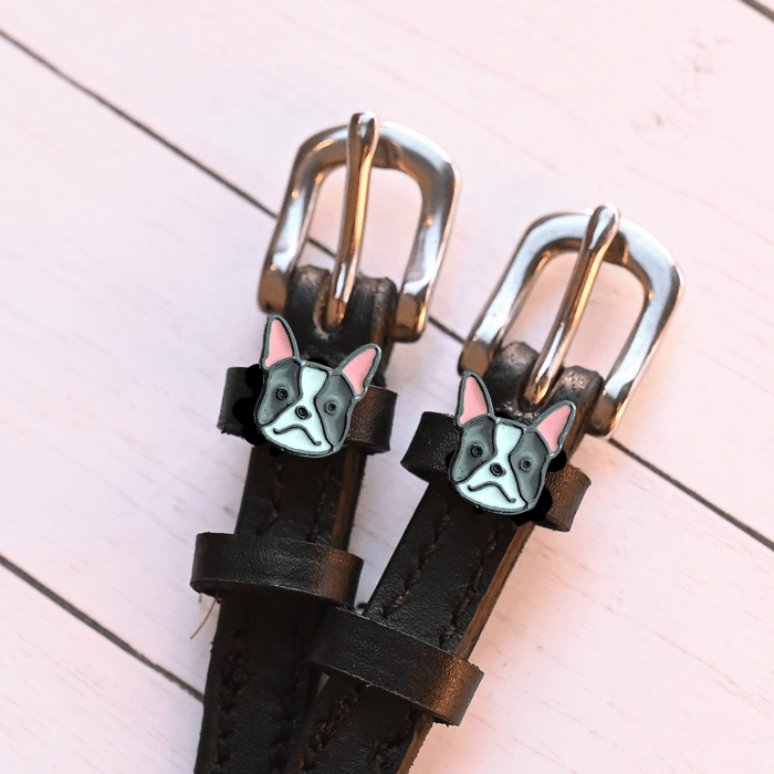Angled close-up of French bulldog charms on ManeJane spur straps over pink planks